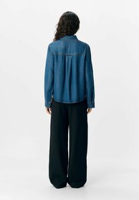 Blå denimskjorta med avslappnad passform, med krage, framparti och rundad nederkant. Matchad med svarta vida byxor.
