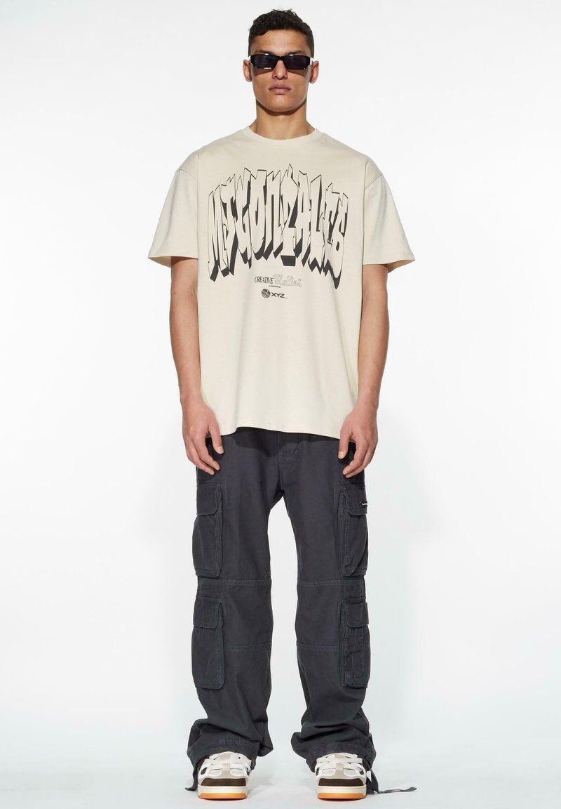 Cream-colored t-shirt with bold black graphic text, paired with dark cargo pants featuring multiple pockets and a relaxed fit.