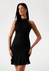 Black lace dress with a fitted design, halter neck, cut-out accents, and a flared hem. Features textured fabric and intricate patterns.