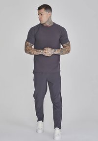 Grijs T-shirt met korte mouwen gecombineerd met bijpassende joggerbroek. De stof lijkt glad en aansluitend, aangevuld met witte sneakers.