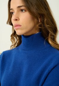 Niebieski sweter w golfie z miękkiego dzianiny, ze żebrowanym kołnierzem i luźnym krojem. Gładka tekstura z minimalnymi detalami, zaprojektowany z myślą o komforcie.