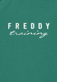 Maglietta di cotone color verde acqua con testo bianco a blocchi "FREDDY" sopra la scritta corsiva "training", realizzata in tessuto liscio e strutturato.