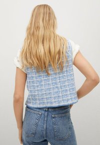 Niebieska kratkowana krótka kamizelka wykonana z tkaniny tkanej, charakteryzująca się pudełkowym kształtem i czystą linią dekoltu, zestawiona z dżinsami o wysokim stanie.