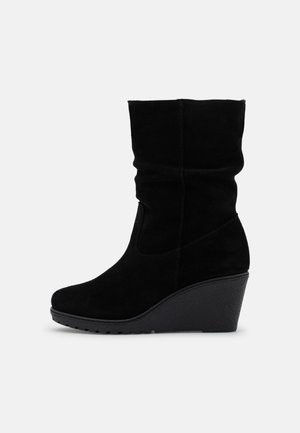 Botte compensée mi-mollet en daim noir avec un bout arrondi et une semelle en caoutchouc texturée sur un fond clair uni.