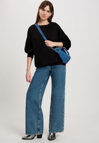 Czarny oversize sweter z szerokimi rękawami, zestawiony z niebieskimi spodniami z szerokimi nogawkami i wysokim stanem. Dodatki to mała niebieska torebka na ramię i błyszczące czarne botki za kostkę.