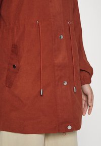 Chaqueta roja ligera con capucha ajustable, cierre de presión y bolsillos laterales. Presenta una textura suave y acentos de hardware en color plateado.