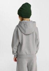 Grå huvtröja med ribbad nederkant och muddar, tillsammans med matchande grå byxor. En grön mössa fulländar outfiten.