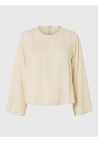 Lys beige langærmet skjorte med rund halsudskæring, diagonale sømme og en tekstureret overflade. Den har en diskret lynlås bagpå.