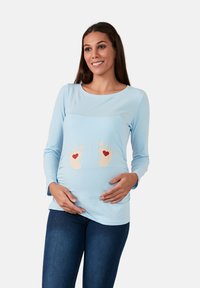 Helles blaues, langärmeliges Stilloberteil mit rundem Ausschnitt, das ein Design aus cremefarbenen Babyfüßen mit roten Herzen in der Taille zeigt.