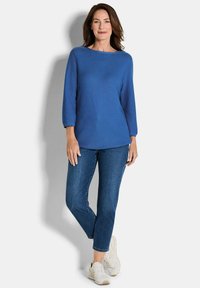 Blauwe trui met lange mouwen en een boothals, gecombineerd met donkerblauwe spijkerbroek en beige sneakers. Eenvoudig ontwerp met een gladde textuur.