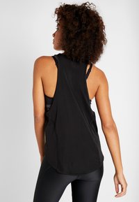 Camiseta sin mangas negra con tejido texturizado, diseño de espalda racer y dobladillo superpuesto. Lleva puesta encima un sujetador deportivo negro; elegante y funcional.