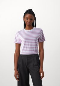 T-shirt en coton rayé violet et blanc avec un col rond et des manches courtes, porté avec un pantalon gris taille haute.