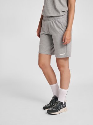 Person iført grå Hummel-shorts, hvide crew-sokker og sort-grå sneakers, stående mod en ensfarvet lys grå baggrund.