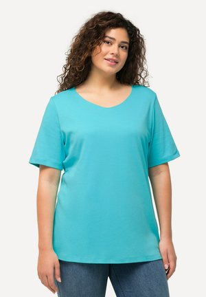T-shirt turchese a scollo a V realizzato in tessuto morbido, caratterizzato da maniche corte e una vestibilità rilassata, abbinato a jeans blu. Nessun motivo o dettaglio visibile.