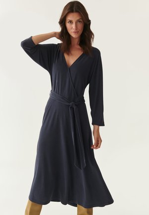 Navy blue wrap dress in soft fabric with a V-neckline, long sleeves, and a tied waist detail. Flowy skirt extends to mid-calf.