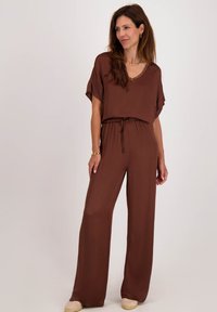 Bruine, korte mouwen jumpsuit met een V-hals en een trekkoord in de taille. Wijde pijpen, gladde stof, zonder zichtbare patronen of accenten.