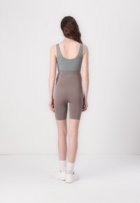 Sleeveless, scoop-back top in light green paired with high-waisted, knee-length brown shorts. Smooth texture, minimal design, plain colors.