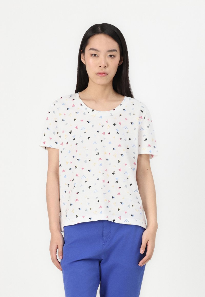 Haut blanc à manches courtes avec un motif géométrique mettant en avant des triangles colorés en rouge, bleu, jaune et noir sur un tissu lisse et léger.