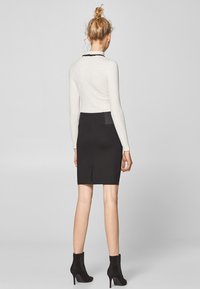 Bílý dlouhý rukáv top s černým lemováním, v kombinaci s černou přiléhavou sukní a černými kotníkovými botami. Sukně má zadní rozparek a kapsu.