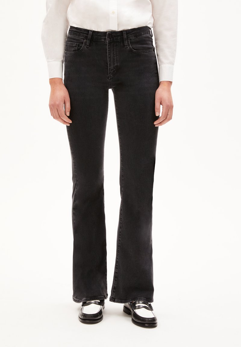 Black denim flared jeans with a mid-rise waistband, five pockets, and a soft texture. Paired with black and white shoes.
