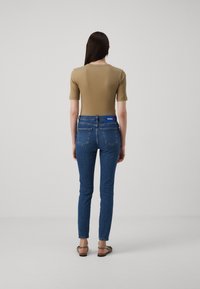 Tynne blå jeans med middels vask, fem-lommers design og en blå logo-patch bak. Kombinert med en beigefarget tettsittende topp og flate sandaler.
