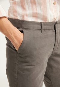 Pantalones gris con una textura suave, con bolsillos laterales y un corte ajustado. Combinados con una camisa de rayas en rosa claro y blanco.
