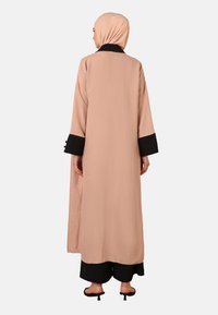 Lang, løs pasform beige abaya med en sort krave og manchetter, lavet af tekstureret stof. Den har en lige skæring og brede ærmer.