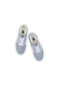 Zapatillas de ante gris con cordones blancos, franja lateral blanca contrastante y un logo en la lengüeta. Textura suave y diseño de puntera redondeada.