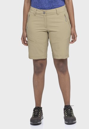 Beige knielange Shorts mit Reißverschlusstaschen, getragen von einer stehenden Person, kombiniert mit dunklen Wanderschuhen und einem blau gemusterten Hemd.