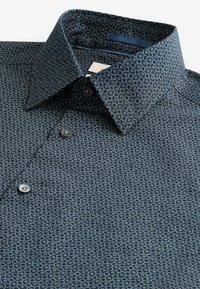 Camisa de botones azul marino con un patrón geométrico, que presenta un cuello extendido, tejido texturizado y botones en contraste.
