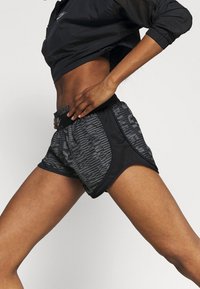 Pantalones cortos deportivos negros con un patrón texturizado en gris, tirantes elásticos y un corte holgado, diseñados para el movimiento y la comodidad.