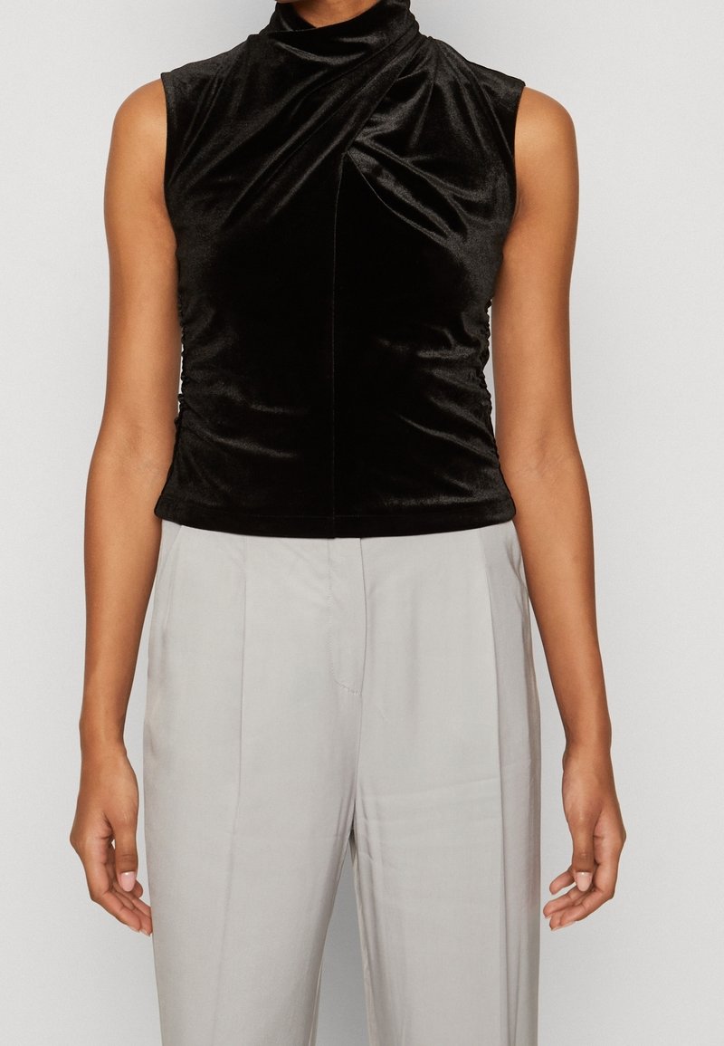 Haut sans manches noir avec un col montant, fabriqué en velours doux. Présente un détail de tissu tordu à l'avant et une silhouette ajustée.
