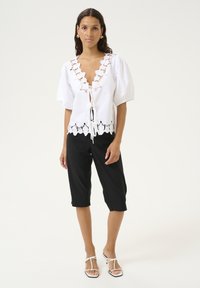 Blusa bianca con maniche a sbuffo e dettagli a taglio lungo il collo e l'orlo, abbinata a pantaloni neri a 3/4 e sandali bianchi con cinturini.