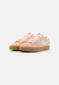 Rozā zamšādas sporta apavi ar gaiši zilu Nike simbolu, gumijas zoli un atbilstošām šņorēm. Iespējama plakana forma un strukturēta augšdaļa.