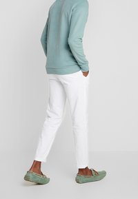 Sudadera azul claro, pantalones blancos y mocasines verdes. Los pantalones tienen bolsillos laterales; los zapatos presentan cordones decorativos y textura.