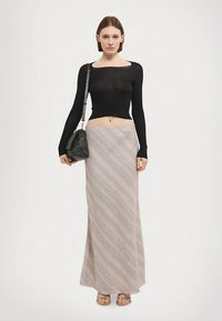 Mustavartinen pitkähihaisen toppi yhdistettynä lattiapituiseen hameeseen, jossa on beigen ja vaaleanruskean vinoraitakuviot. Mukana musta käsilaukku.