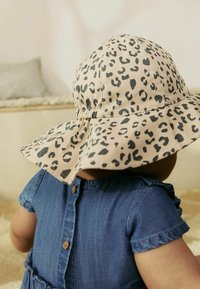 Chapeau rond et souple en beige avec un motif léopard noir ; tissu doux avec une couronne froncée, associé à une robe en denim avec des boutons.