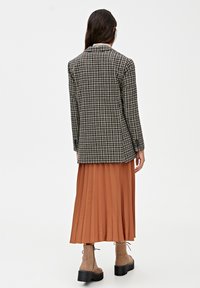 Blazer a quadri bianco e nero, abbinato a una gonna plissettata di colore ruggine. Il blazer presenta un colletto a rever e una linea dritta.