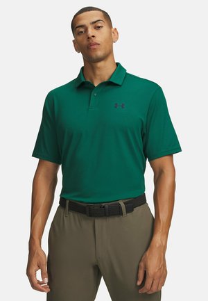 Man wearing a dark green short-sleeve polo shirt with a small logo and olive pants with a black braided belt.