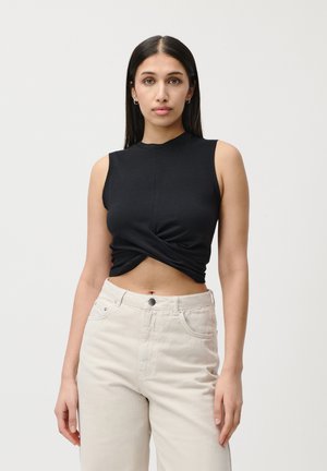 Svart kortermet topp uten ermer med et vridd design foran, sammen med høyt liv, lyse beige bukser med knapplukking.