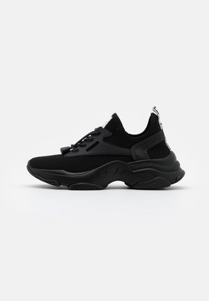 Zwarte sportief schoenen met een bovenwerk van mesh, gevoerde kraag en een gestructureerde zool. Heeft een vetersluiting en een treklipje bij de hiel.
