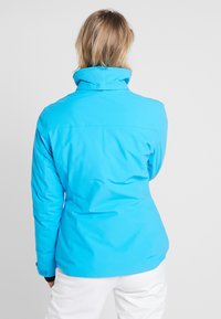 Blå vattentät jacka med hög krage och slät textur, med en figursydd design och långa ärmar, sedd bakifrån.