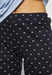 Zwarte broek met een aansluitend ontwerp en een wit bloemenpatroon. Gemaakt van een zachte stof met zichtbare stiksels bij de tailleband.