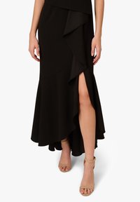 Czarna, dopasowana spódnica z falbaną na końcu i bocznym rozcięciem, wykonana z teksturowanej tkaniny. Połączona z cielistymi sandałami na kostkę.