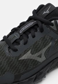 Černé a šedé trailové běžecké boty Mizuno Wave Lur GX s texturovanou tkaninou, tkaničkami a logem na boku a jazyku.