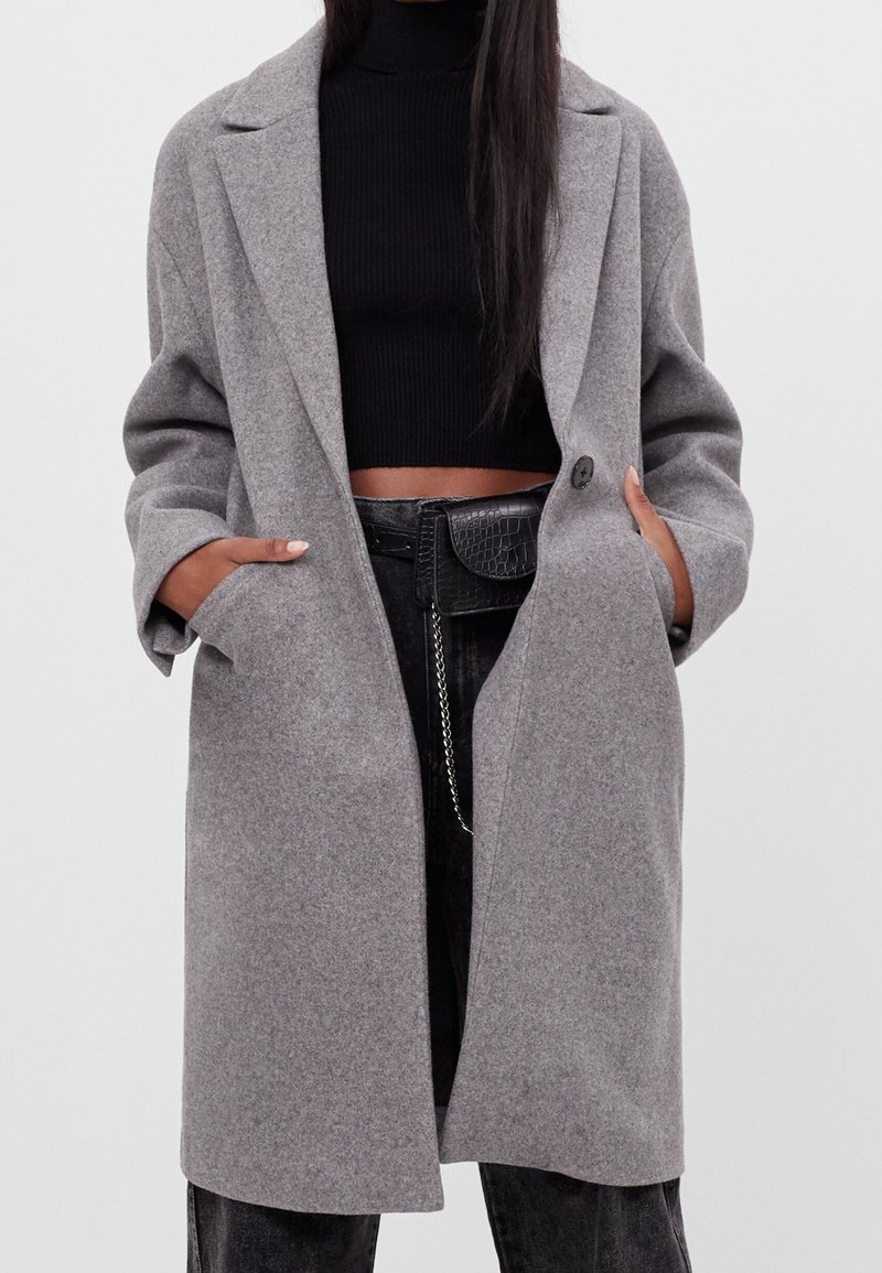 Šedý kabát z vlněné směsi s klopovým límcem, předním zapínáním na knoflíky a bočními kapsami. Texturovaná tkanina s pohodlným střihem a dlouhými rukávy.