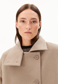 Beige wool coat with a high collar, two large buttons, and a soft texture. Features a clean design and a relaxed fit, suitable for layering.