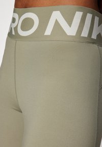 Leggings verde oliva con una amplia cinturilla elástica que presenta "PRO NIKE" en blanco. Textura suave y diseño ajustado para mayor comodidad.