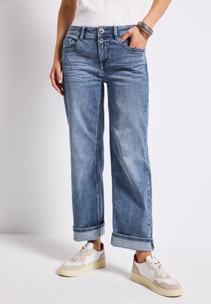Light wash, loose-fit denim jeans with rolled cuffs, five pockets, and metal button details, paired with cream sneakers.