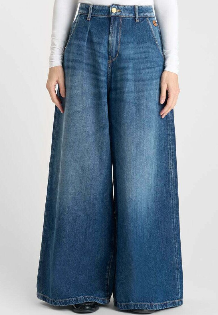 Pantalones de mezclilla de pierna ancha en azul medio, con una cintura alta, frente plisado y una textura suave. Terminados con un cierre de botón.